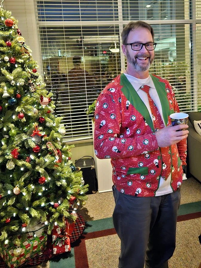 Staff member celebrating in holiday attire by a Christmas tree.