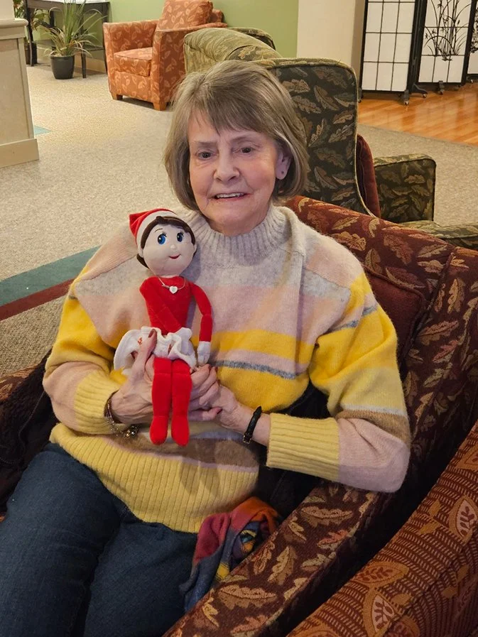 Resident holding a doll in a cozy lounge.