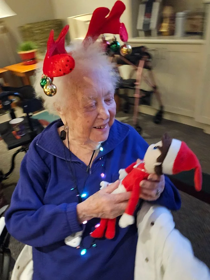 Elderly resident wearing festive attire, holding a plush toy.