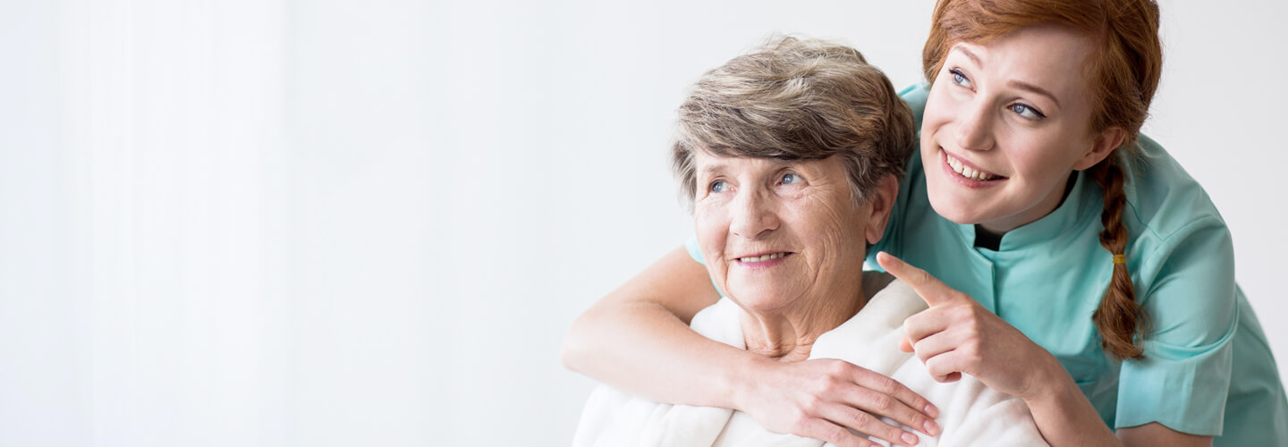 A caregiver with an elderly woman in a bright room.
