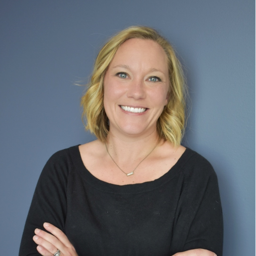 Smiling woman with crossed arms against a blue wall.
