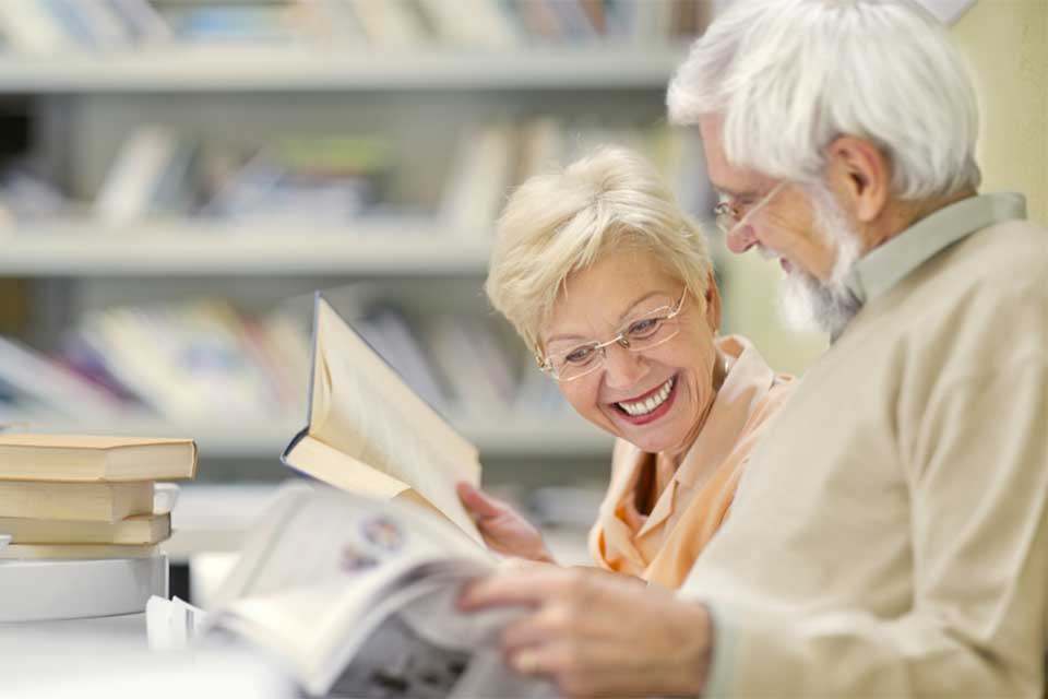 Two seniors enjoying reading books in a library