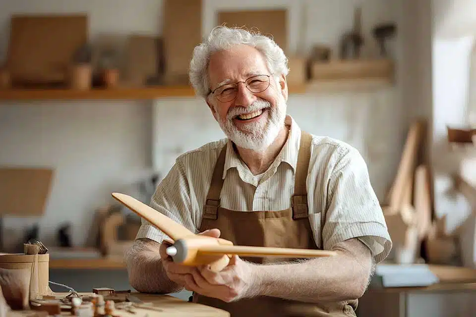 Elderly man happily crafting wooden airplane model