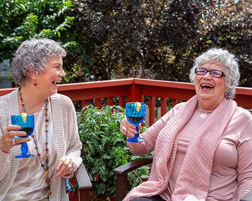 Two women laughing and enjoying drinks on a patio