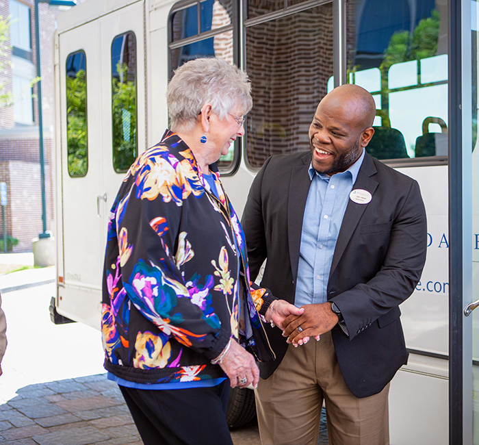 Staff member greeting a resident by a facility shuttle