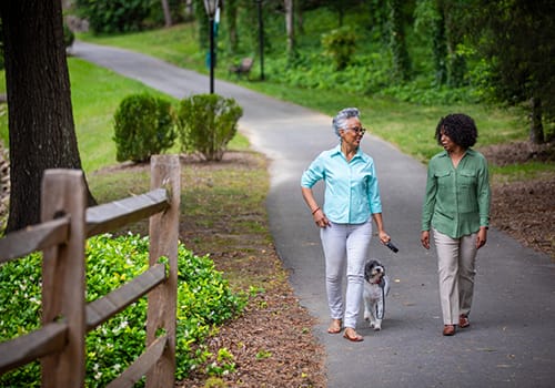 Two women walking a dog on a pathway