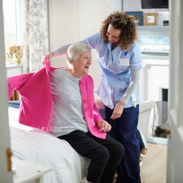 A caregiver assisting an elderly woman indoors.