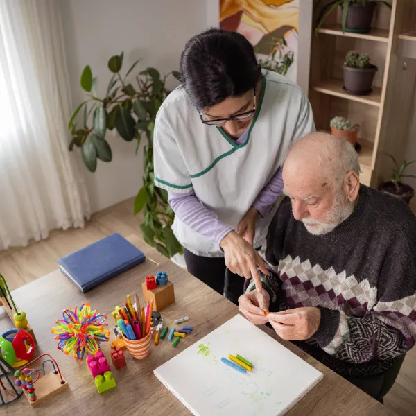 Caregiver assisting senior with art activity.