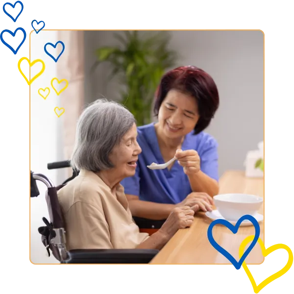 Caregiver feeding a senior resident at a table.