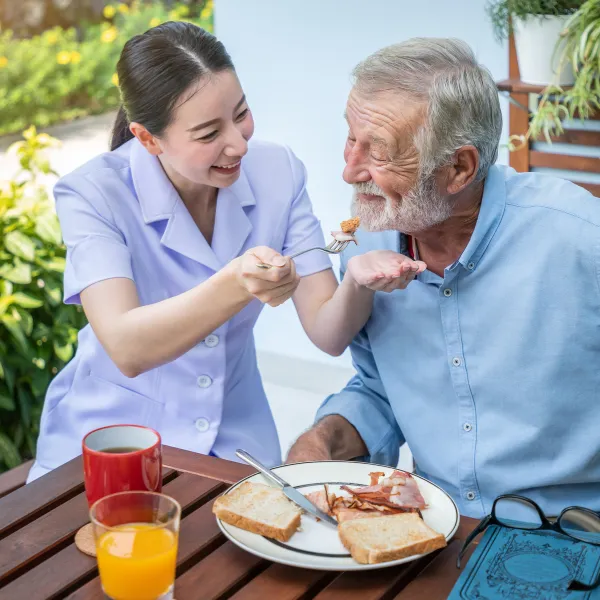 Staff member serving food to a senior man outdoors.
