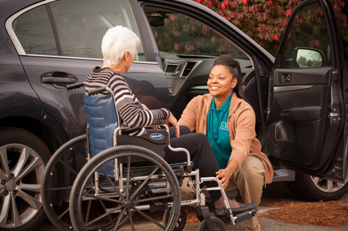 Caregiver assisting woman in wheelchair from vehicle