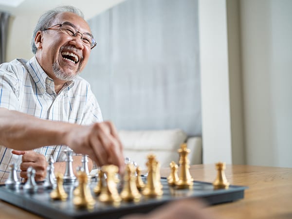 An older man joyfully playing chess in a common area
