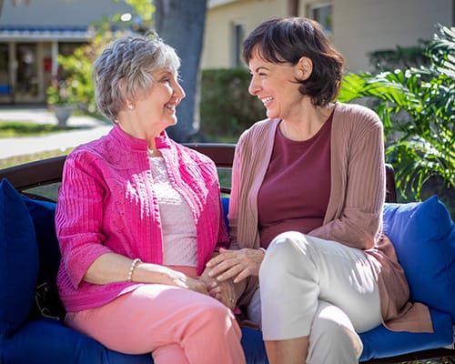 Two women smiling and enjoying each other's company on a bench