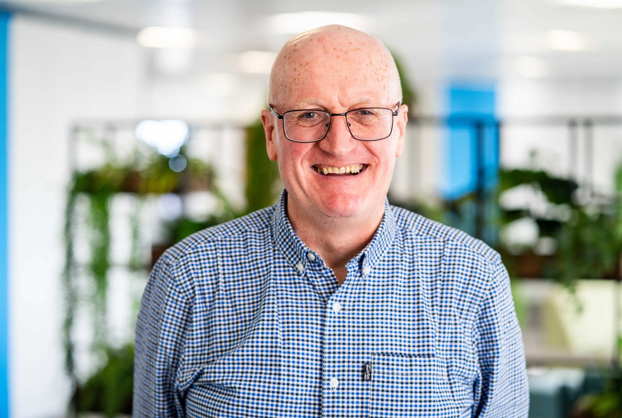A smiling man in a checked shirt in a bright interior space