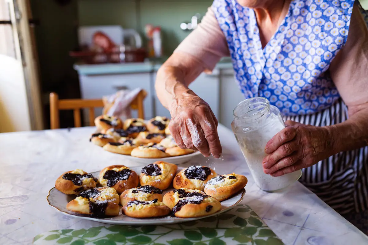 An elderly woman preparing pastries in a cozy kitchen.