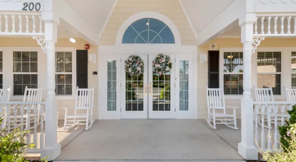 Entrance of a senior living facility with rocking chairs and floral decor