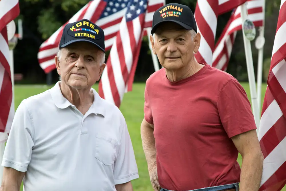 Two veterans wearing hats in a park with flags