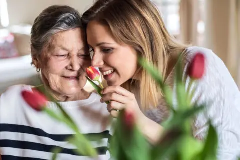 A resident and staff member smelling a flower together