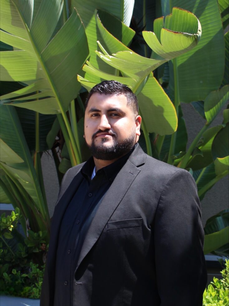 A staff member posed outdoors in front of tropical plants