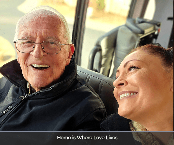 A resident and staff member smiling together in a transportation vehicle.