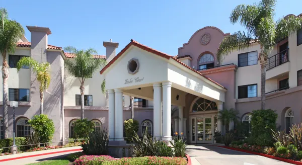 Entrance of a senior living facility with palm trees and flowers