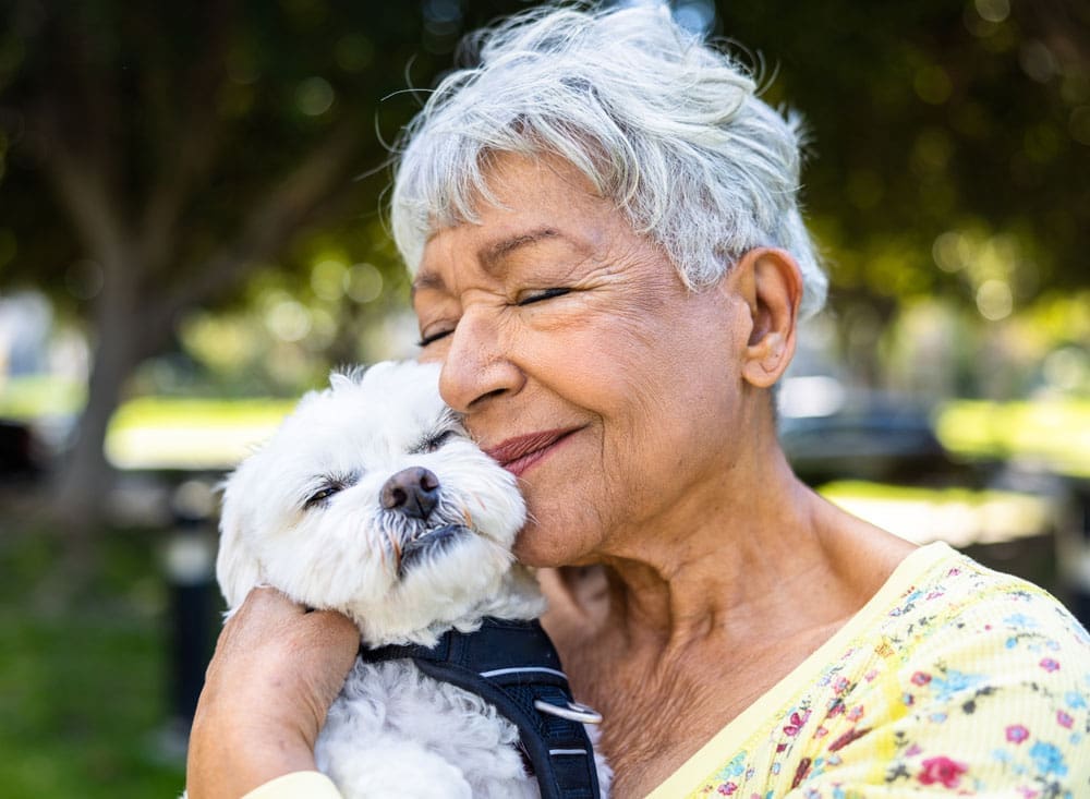 A happy resident hugging a small dog in a park