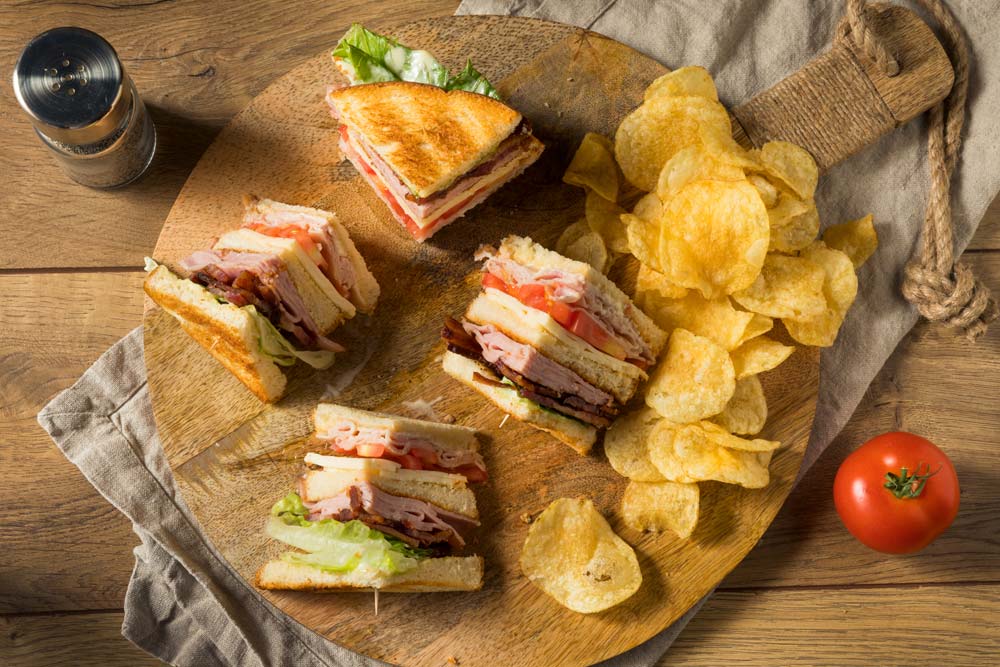A club sandwich with chips on a wooden board
