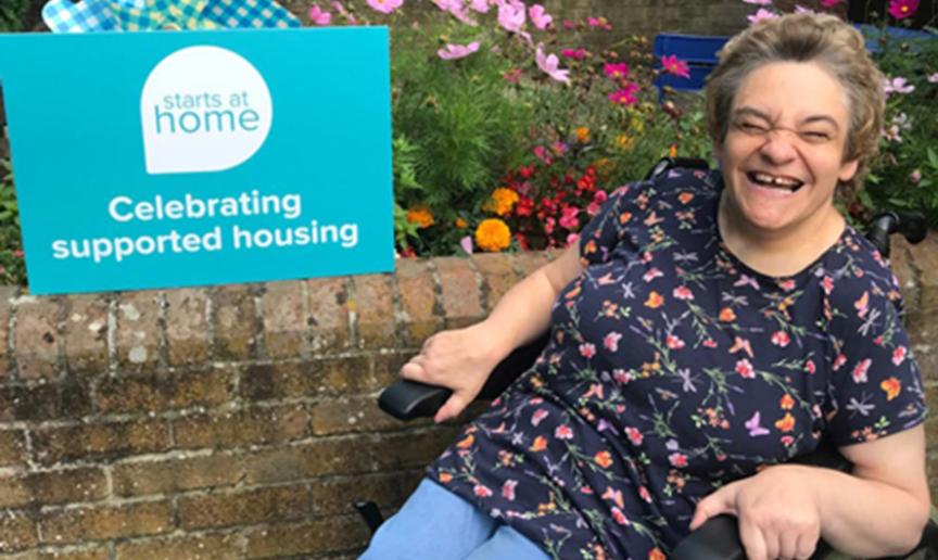 Resident in a wheelchair smiling outdoors near flower bed