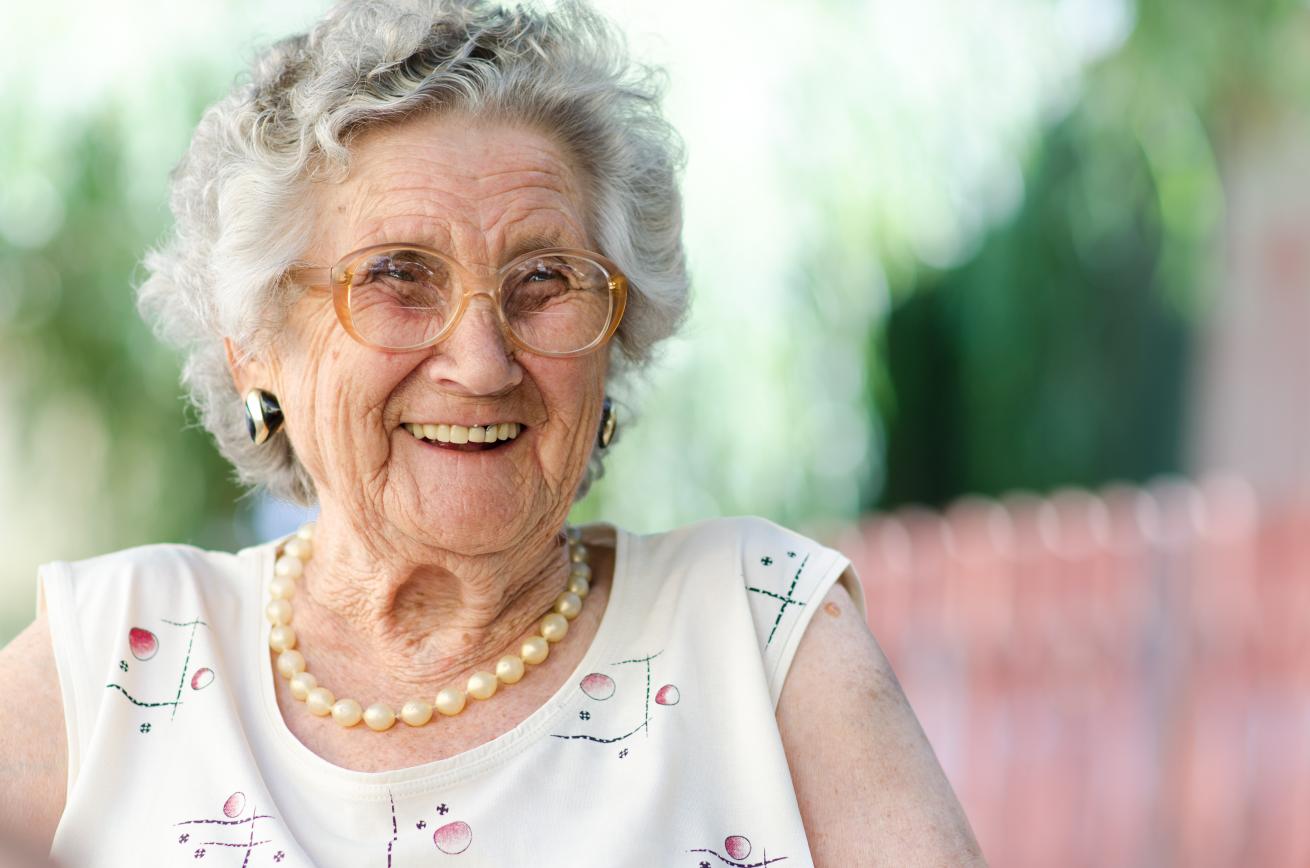 An elderly woman smiling joyfully outdoors