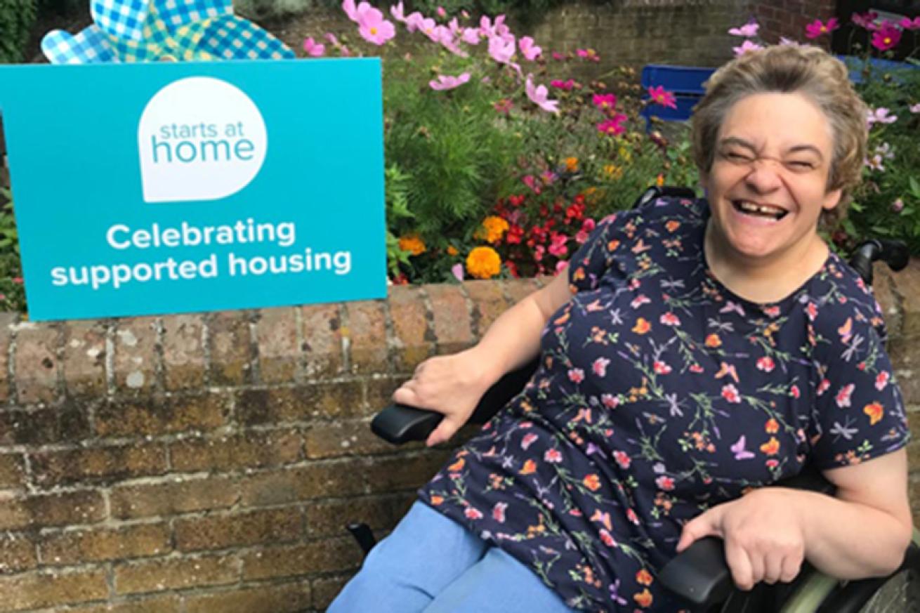 Resident in a garden area smiling next to a sign