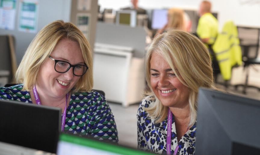 Two staff members smiling while working at computers in an office