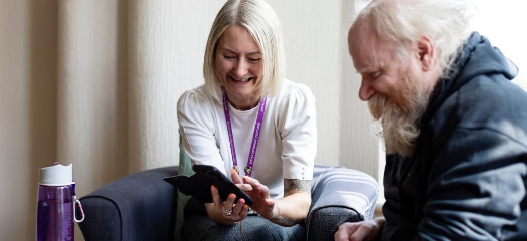 Staff member showing a phone to a resident in a cozy setting