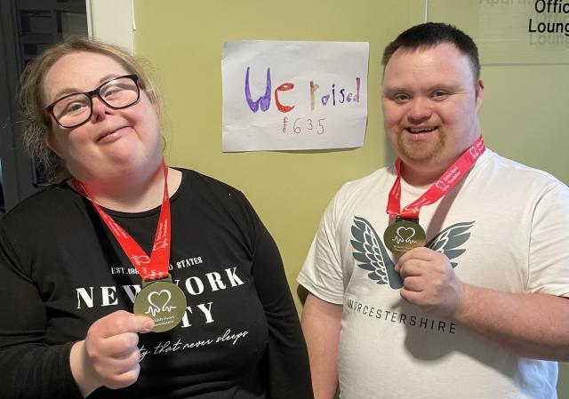 Two residents with medals in front of a fundraising sign
