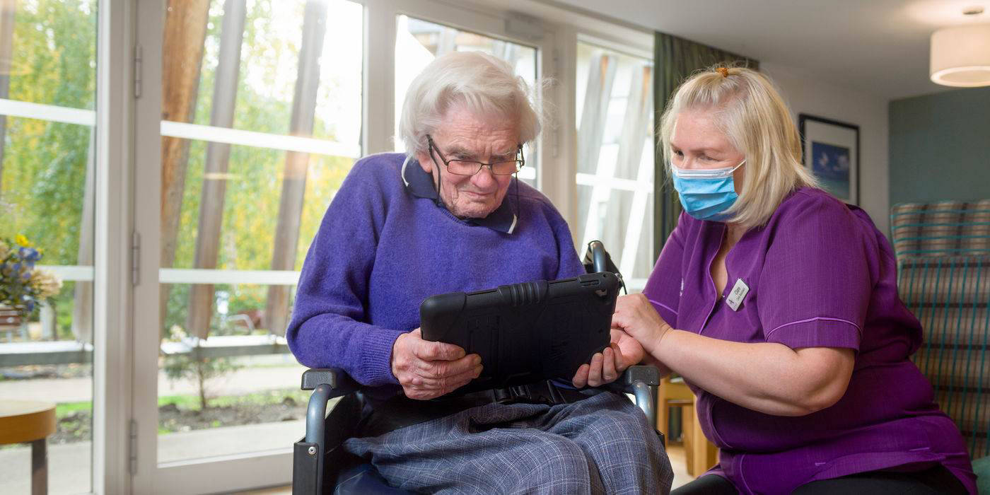 Caregiver assisting a senior woman with a tablet
