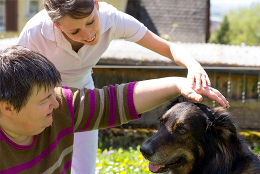 Resident interacting with staff and a dog outdoors.