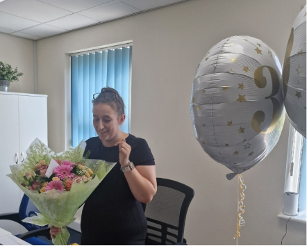 Staff member celebrating with flowers and balloons.