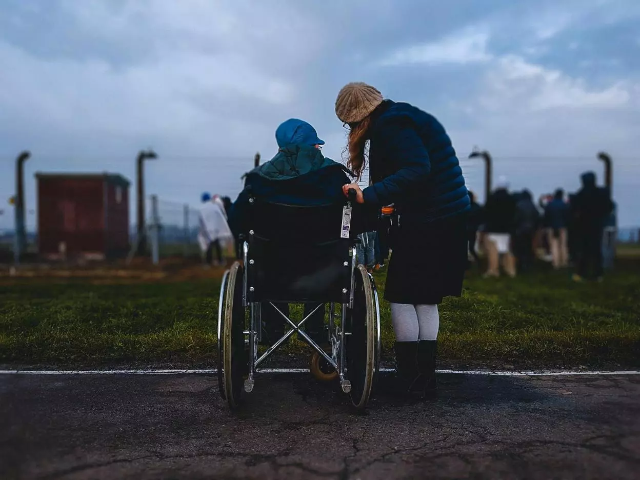 Person assisting a resident in a wheelchair outdoors.