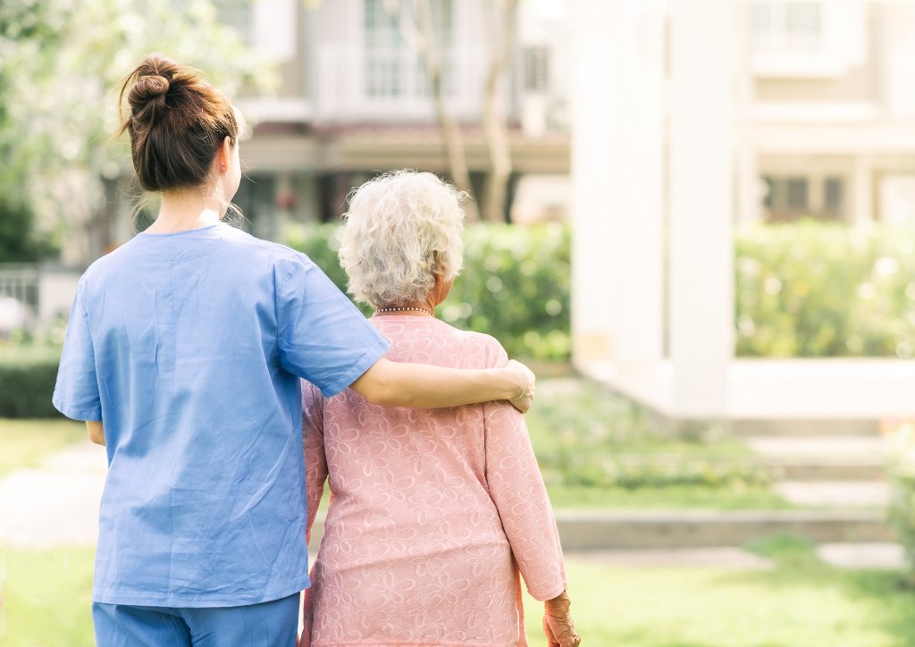 Caregiver assisting elderly resident outdoors.