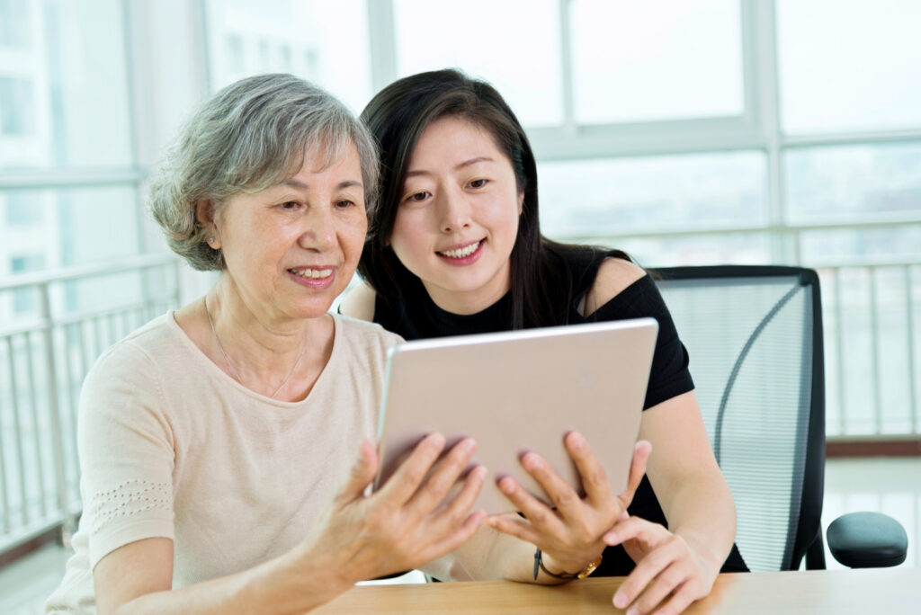 Two women interacting with a tablet in a bright space.