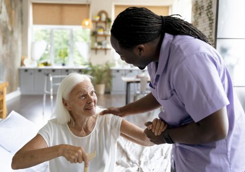 A caregiver interacting with an elderly woman in a room.