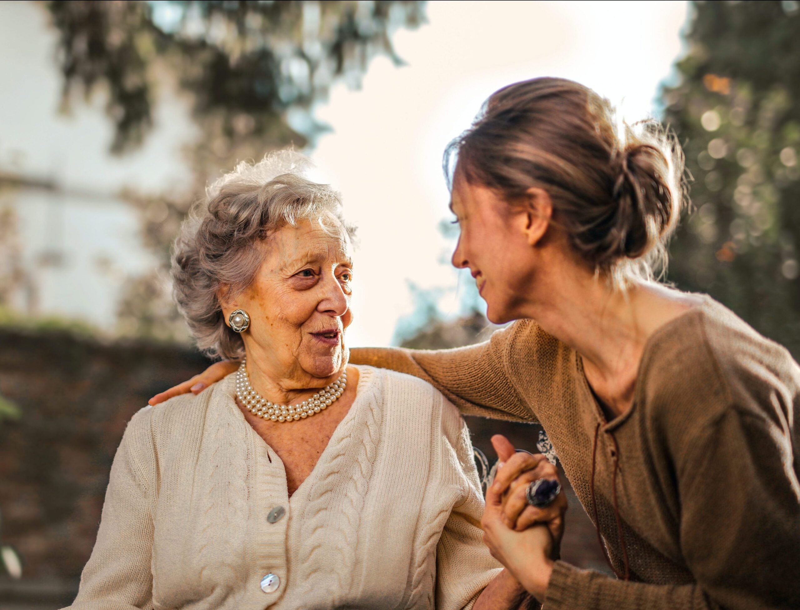 An elderly woman and caregiver sharing a joyful moment outdoors.