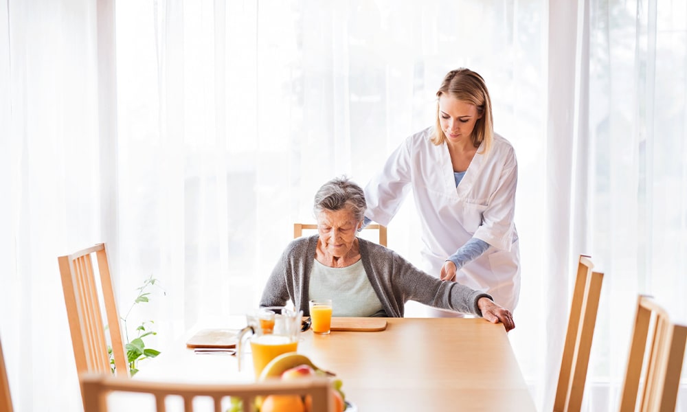 Caregiver assisting an elderly resident at a table.