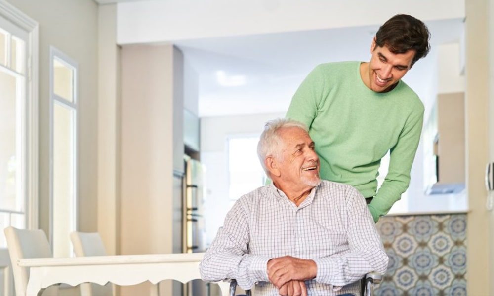 A caregiver assisting an elderly man in an interior setting.