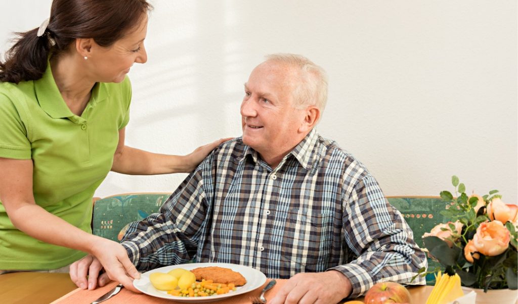 Staff serving a meal to a resident in a dining area.