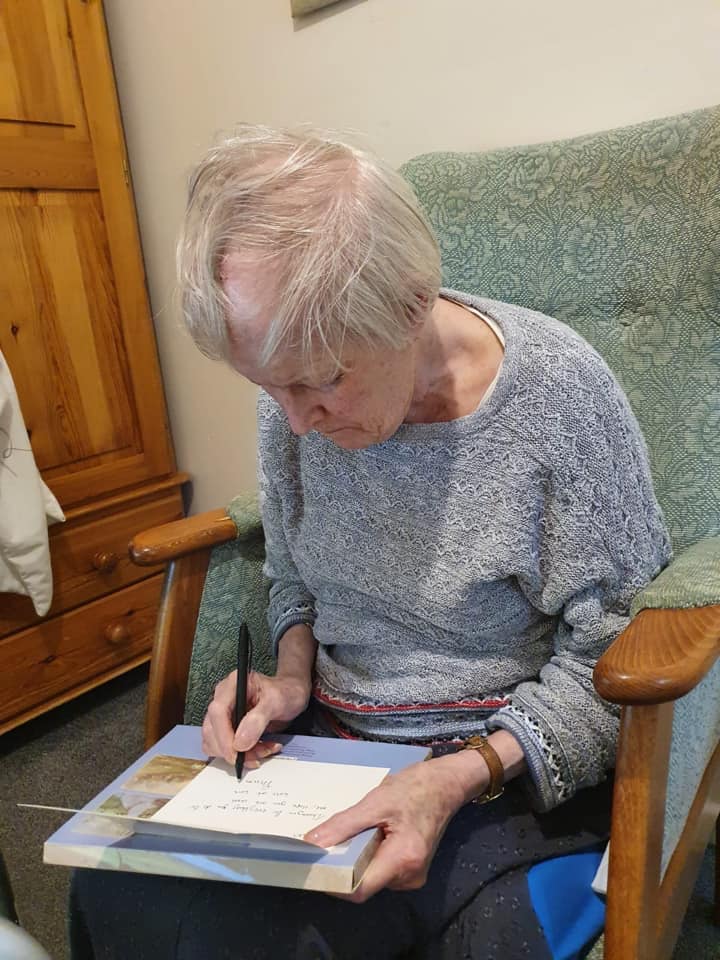 Elderly woman writing in a cozy environment.
