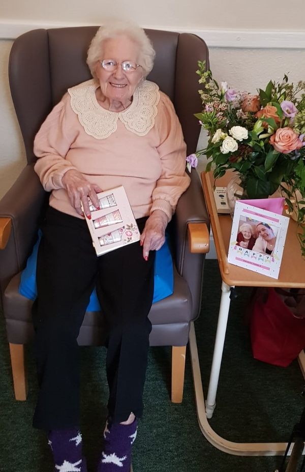 Elderly woman holding a card in a cozy chair.