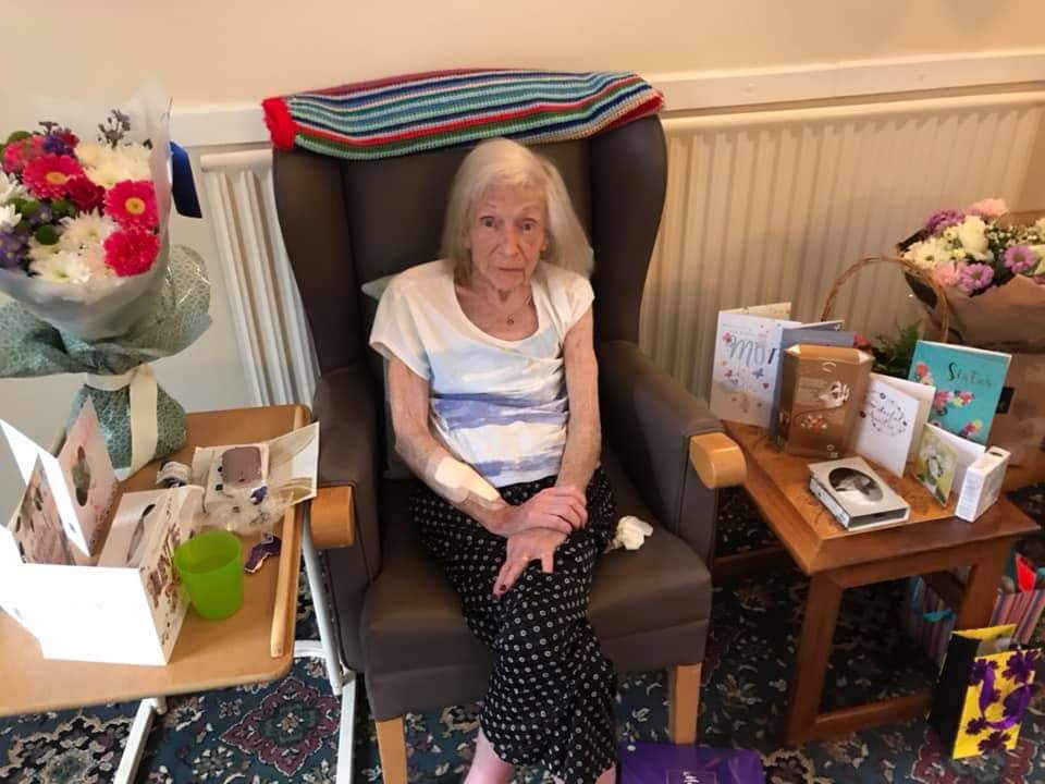 Elderly woman sits in chair among decorations.