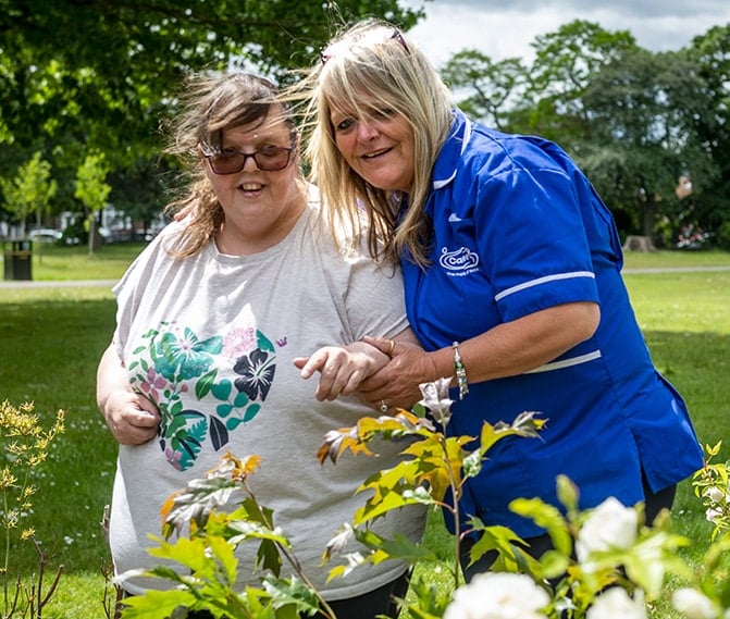 Care staff assisting a resident outdoors in a garden