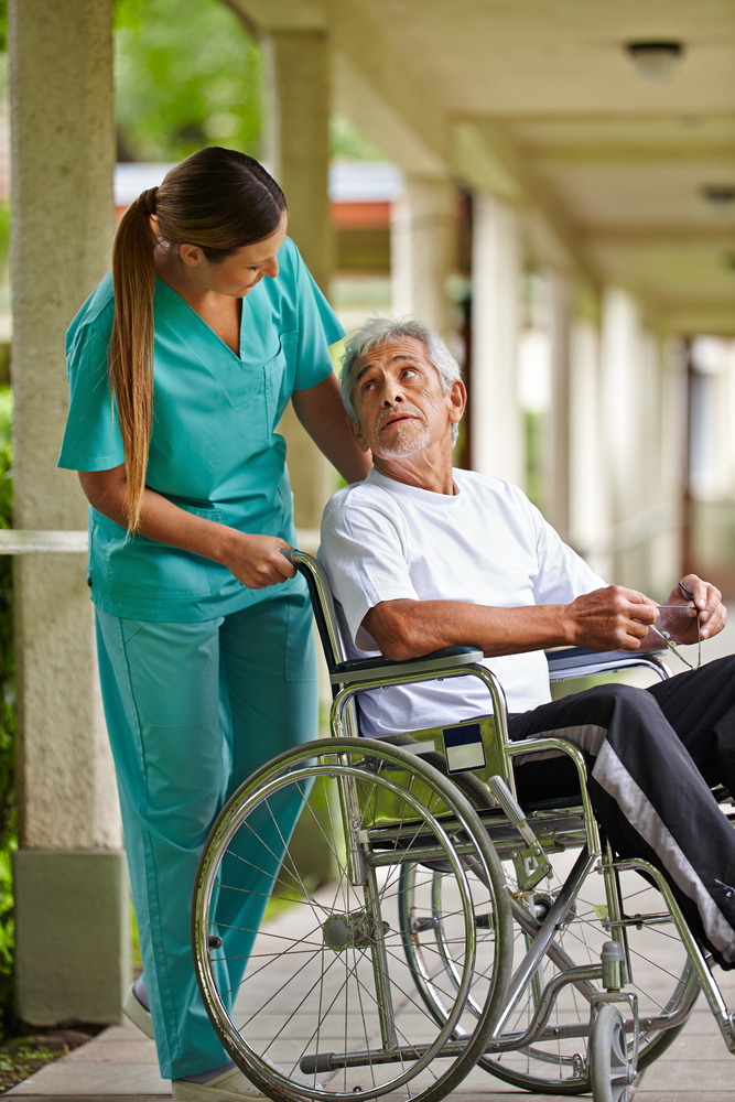 Nurse assisting a senior man in a wheelchair outdoors