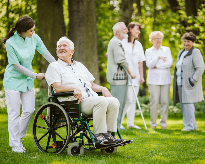 Elderly man in a wheelchair with caregiver outdoors.